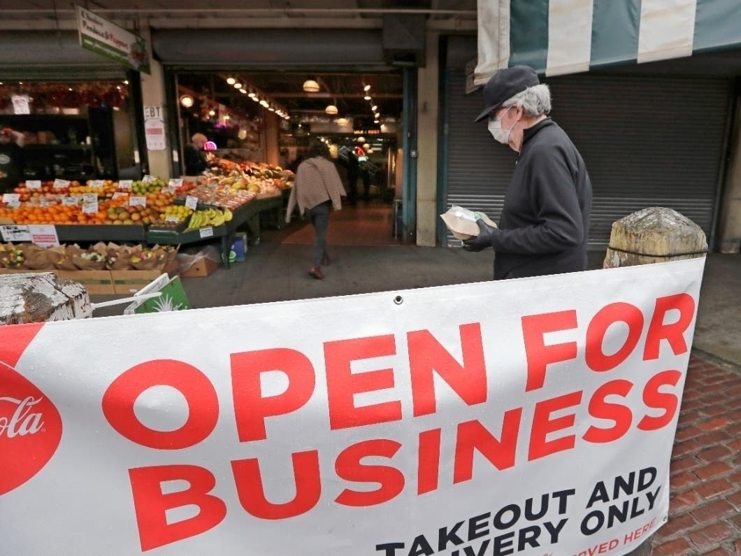 A man wearing a face mask carries a takeout meal as he walks through the Pike Place Market during the coronavirus outbreak Saturday, May 2, 2020, in Seattle. 