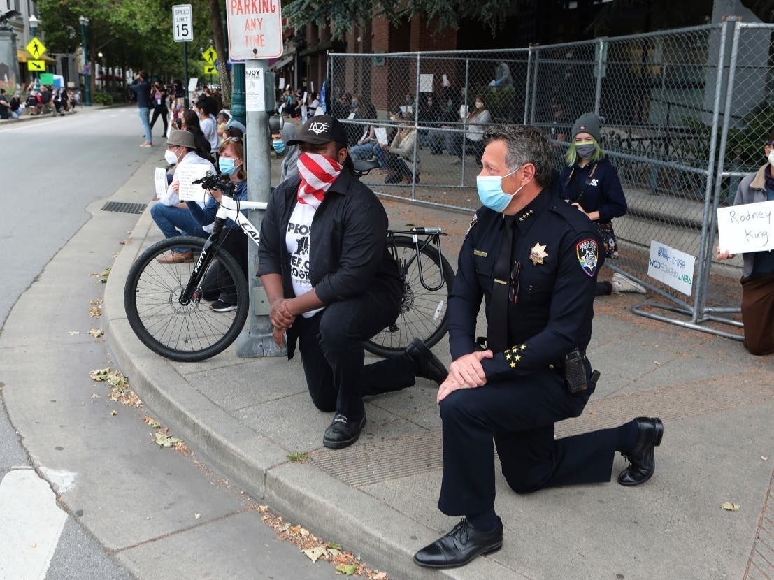 Santa Cruz, Calif., Police Chief Andy Mills, right, and Santa Cruz Mayor Justin Cummings, center, take a knee along with hundreds gathered on Pacific Avenue in downtown Santa Cruz on Saturday May 30, 2020 to honor the memory of George Floyd.