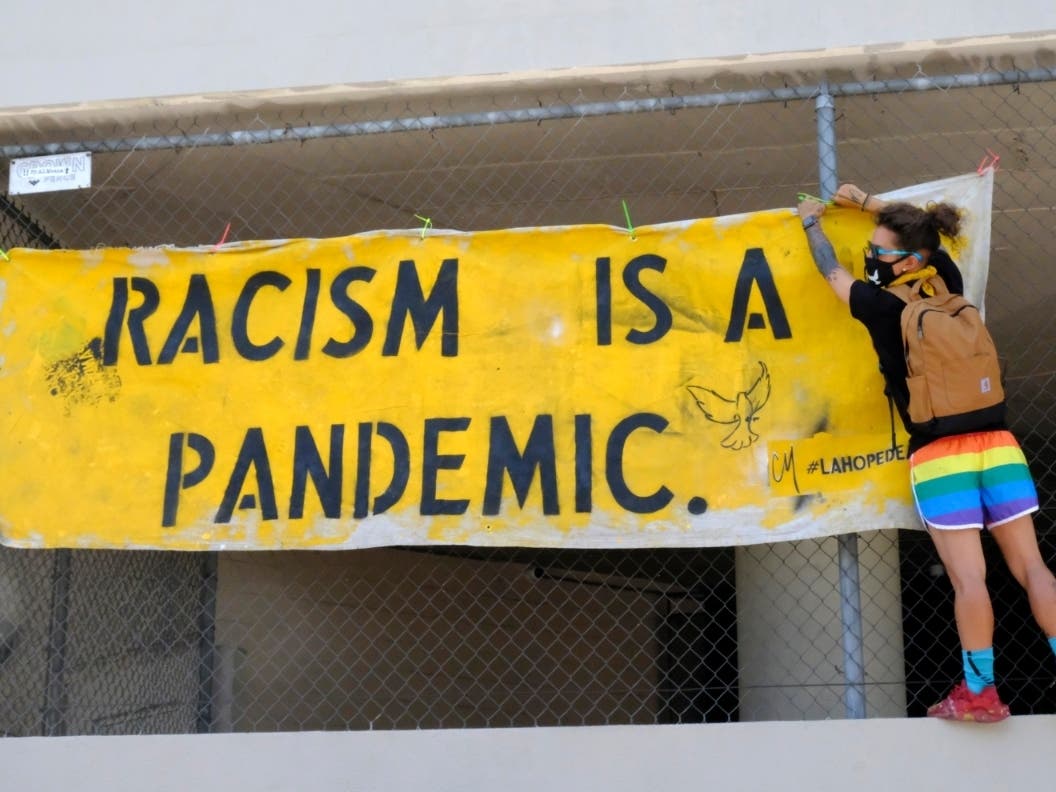 A protester hangs a sign stating "Racism is a Pandemic" at the All Black Lives Matter march, organized by black LGBTQ+ leaders, on Sunday, June 14, 2020, in Los Angeles.