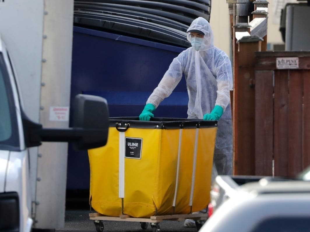 A member of a cleaning crew wheels a cart toward a vehicle at the Life Care Center, where at least 35 coronavirus deaths have been linked to the facility, Wednesday, March 18, 2020, in Kirkland, Wash.