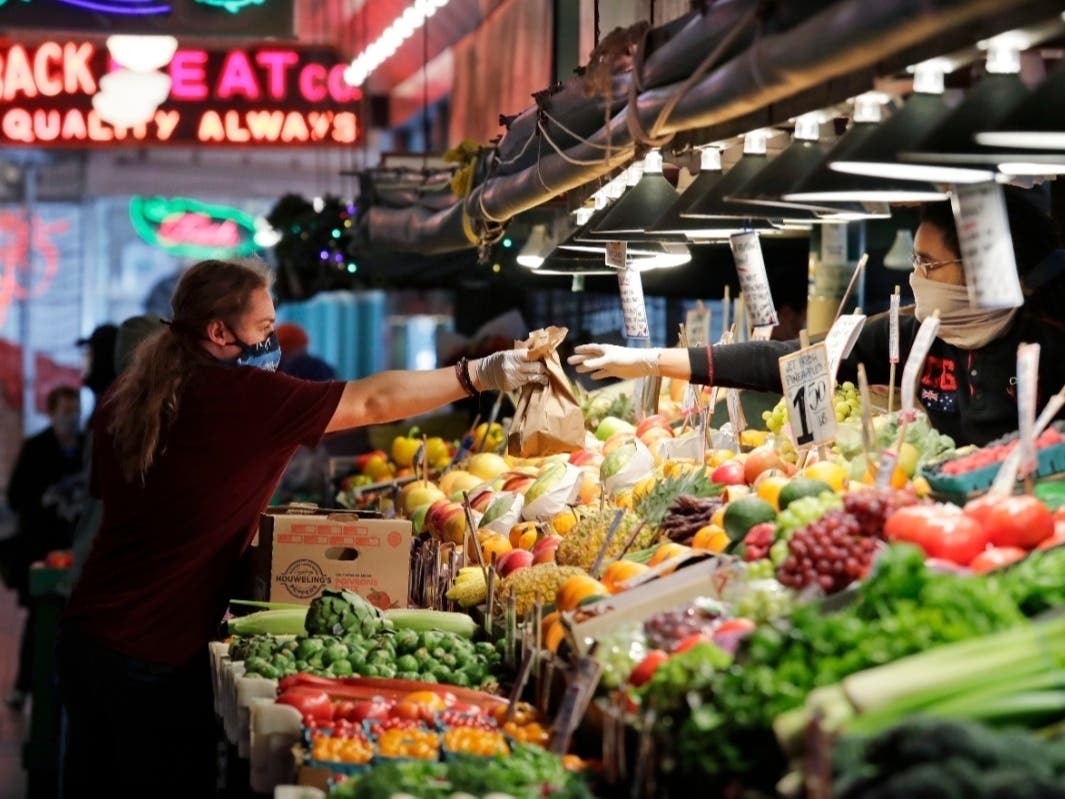 One vendor hands bagged produce to another at a vegetable stand at Pike Place Market still open during the coronavirus outbreak Saturday, May 2, 2020, in Seattle.
