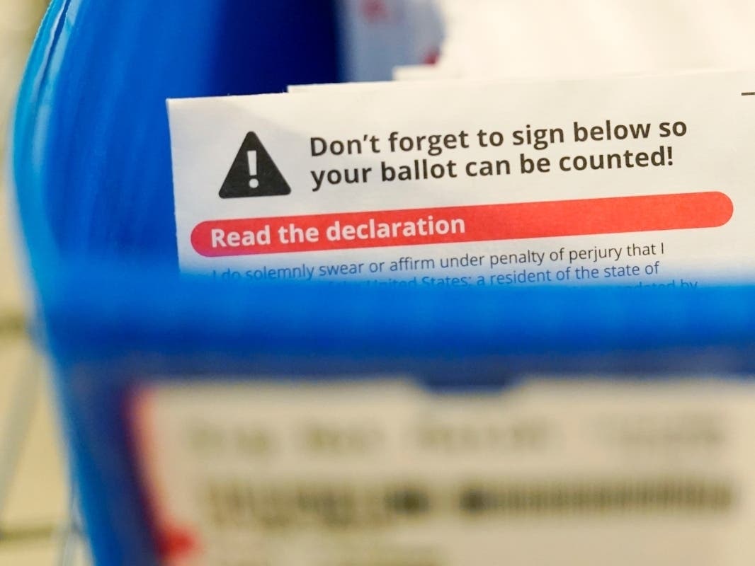 A reminder that voters need to sign their ballots is shown in a box of ballots awaiting signature verification at the King County election headquarters in Renton, Wash., Friday, Oct. 23, 2020.
