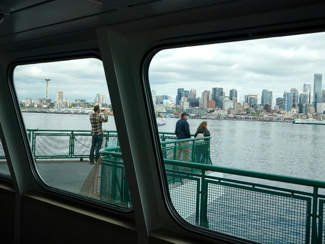 Passengers stand on an outside deck while riding on a Washington state ferry from Bremerton to Seattle, Tuesday, May 25, 2021, in Seattle, Wash.