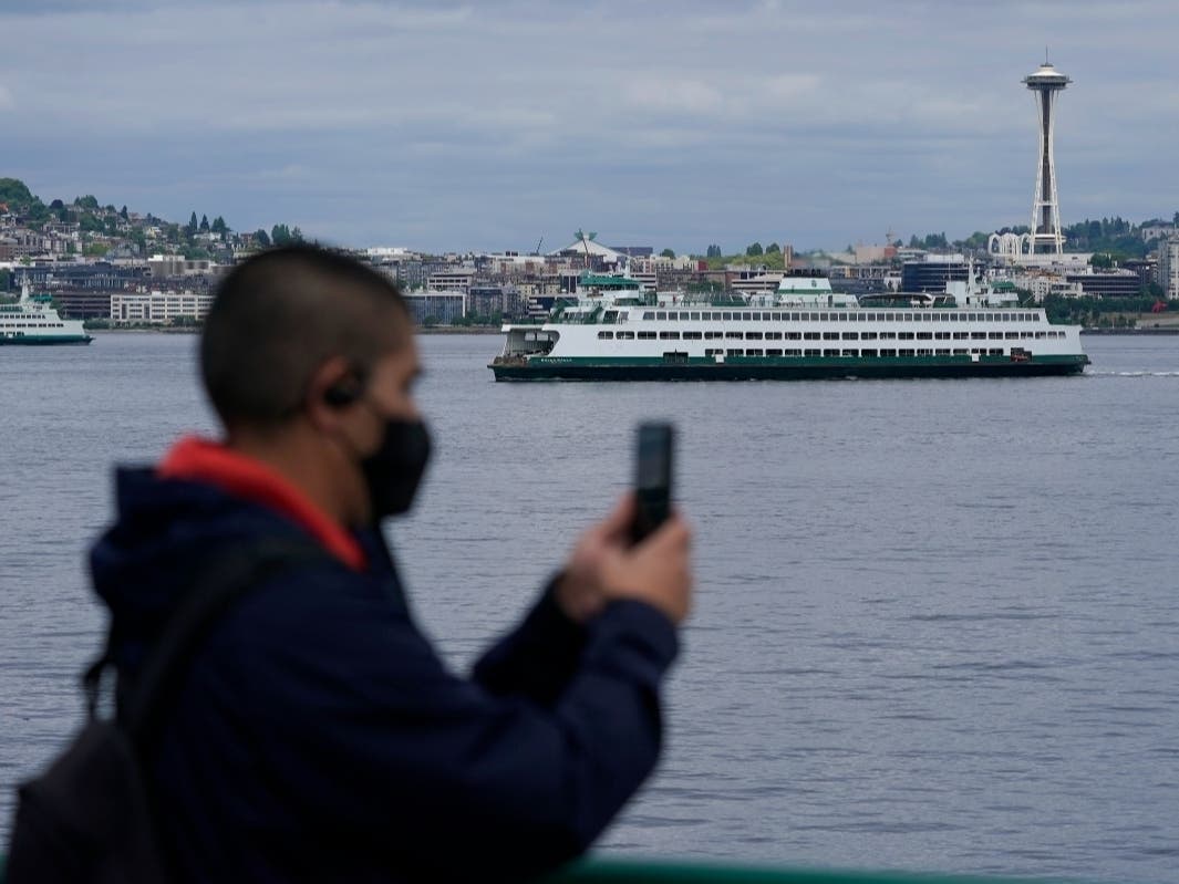 A passenger wears a mask while riding on a Washington state ferry from Bremerton to Seattle as another ferry passes near the Space Needle, Tuesday, May 25, 2021, in Seattle.