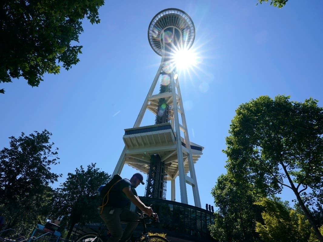 A cyclist passes by as the sun shines behind the Space Needle, Monday, June 28, 2021, in Seattle.
