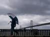 A pedestrian carries an umbrella while walking in front of the San Francisco-Oakland Bay Bridge in San Francisco, Tuesday, March 21, 2023.