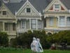 Pedestrians wearing ponchos walk down a path at Alamo Square Park in front of the "Painted Ladies," a row of historical Victorian homes, in San Francisco, Tuesday, March 21, 2023.