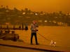 A man walks his dog along Bridgeway Avenue as smoke from wildfires darken the morning Wednesday in Sausalito.