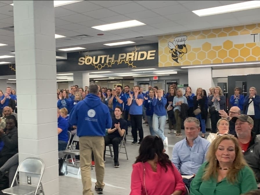 Blue-shirted teachers and other audience members on Thursday applaud John Bowman (walking), co-president of the teachers union, after he finishes his speech denouncing the school board. To the right are the board's defenders, who withheld their applause. 