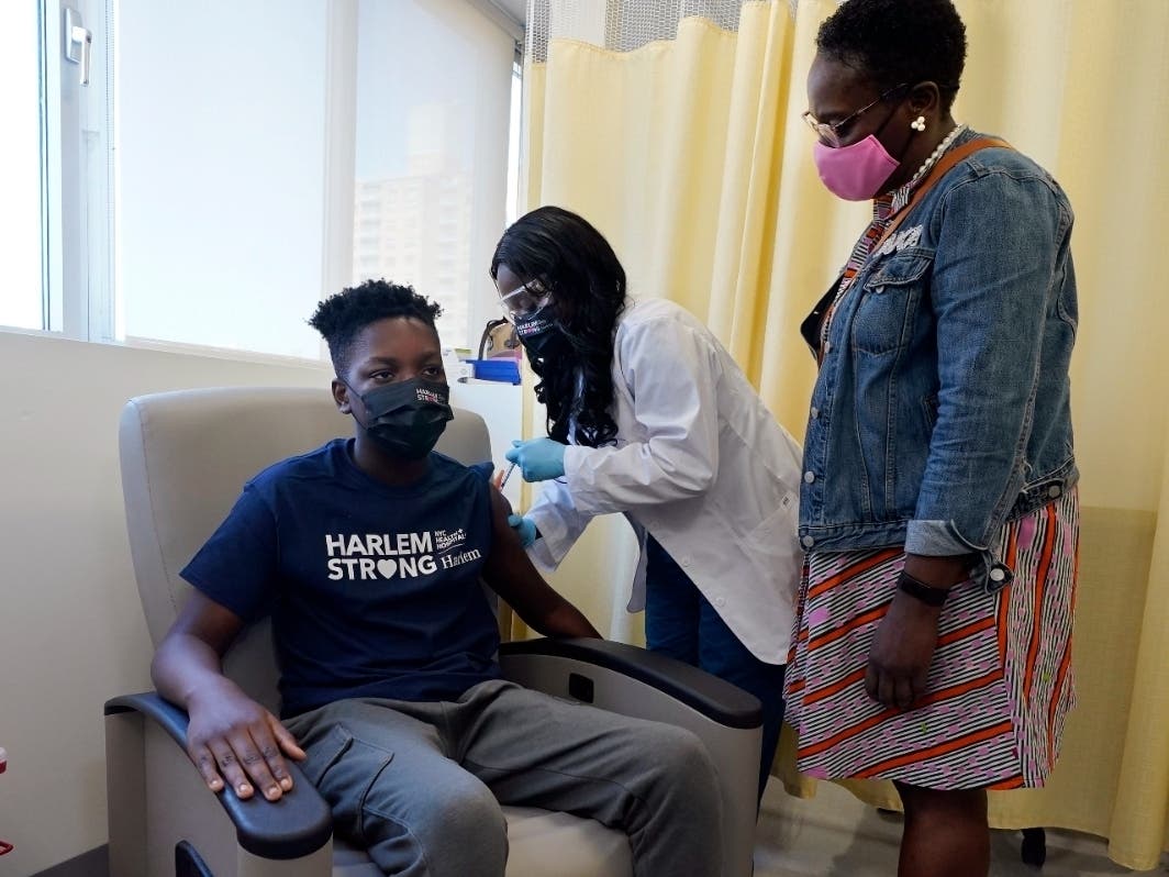 Julian Boyce, 14, receives his first Pfizer COVID-19 vaccination at NYC Health + Hospitals/Harlem, from nurse Kenia Georges, center, as his mother Satrina Boyce stands by on May 13.