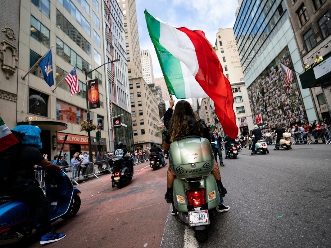 A motorist riding on the back of a scooter waves an Italian flag as a group rolls up Fifth Avenue during the Columbus Day parade Monday.