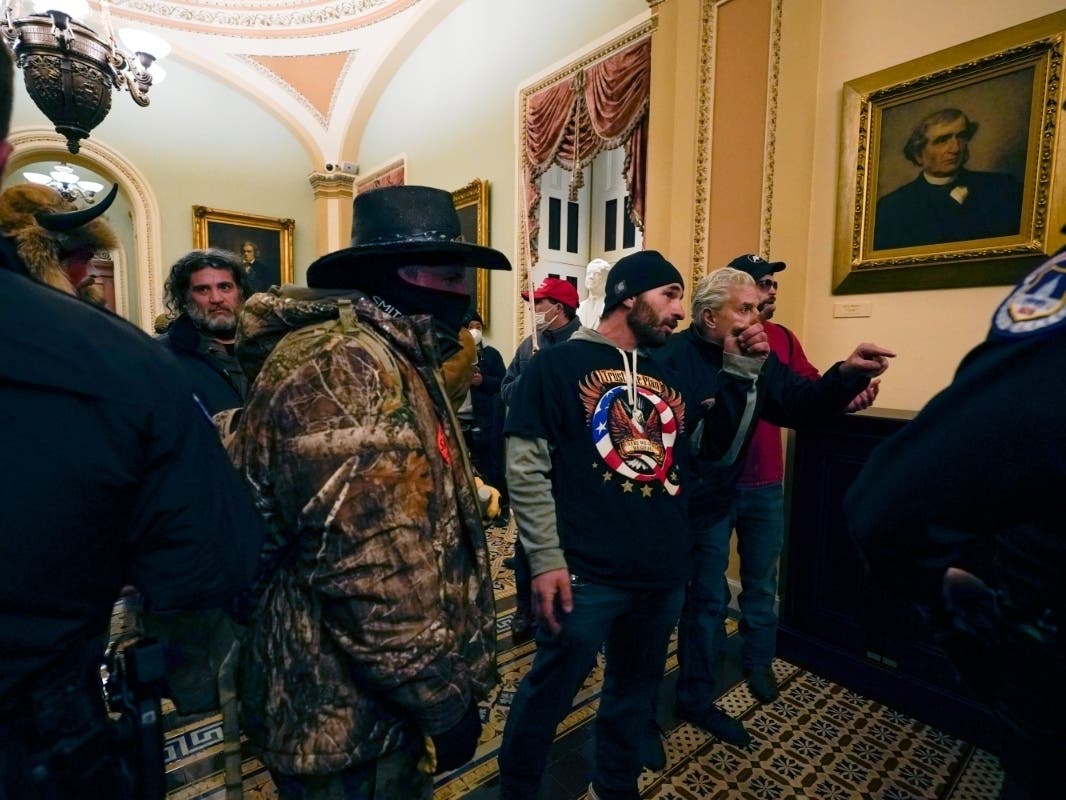 Protesters walk as U.S. Capitol Police officers watch in a hallway near the Senate chamber at the Capitol in Washington, Wednesday, Jan. 6, 2021, near the Ohio Clock.
