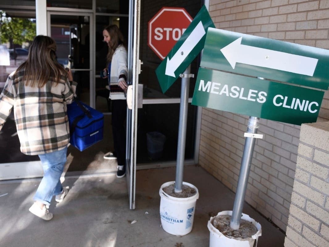 Health department staff members enter the Andrews County Health Department measles clinic carrying doses of the measles, mumps and rubella vaccine, April 8, 2025, in Andrews, Texas.