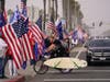 A man carrying a surfboard passes through supporters of President Donald Trump Wednesday, Jan. 6, 2021, in Huntington Beach, Calif. 