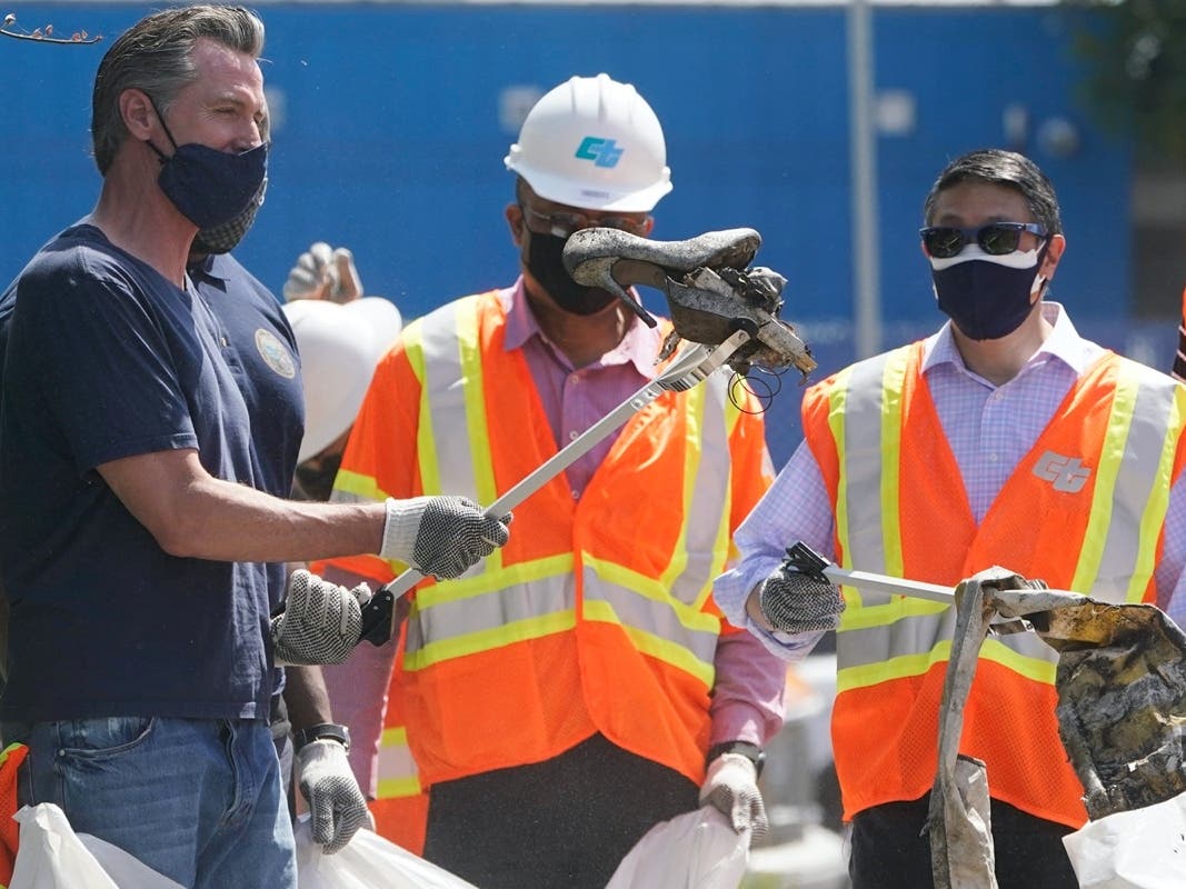 In this Tuesday, May 11, 2021, file photo, California Gov. Gavin Newsom reacts as he finds a pair of old high heel shoes as he joins a cleanup effort in Los Angeles. 