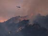 A firefighting helicopter flies away after dropping water over a brush fire scorching at least 100 acres in the Pacific Palisades area of Los Angeles Saturday, May 15, 2021.