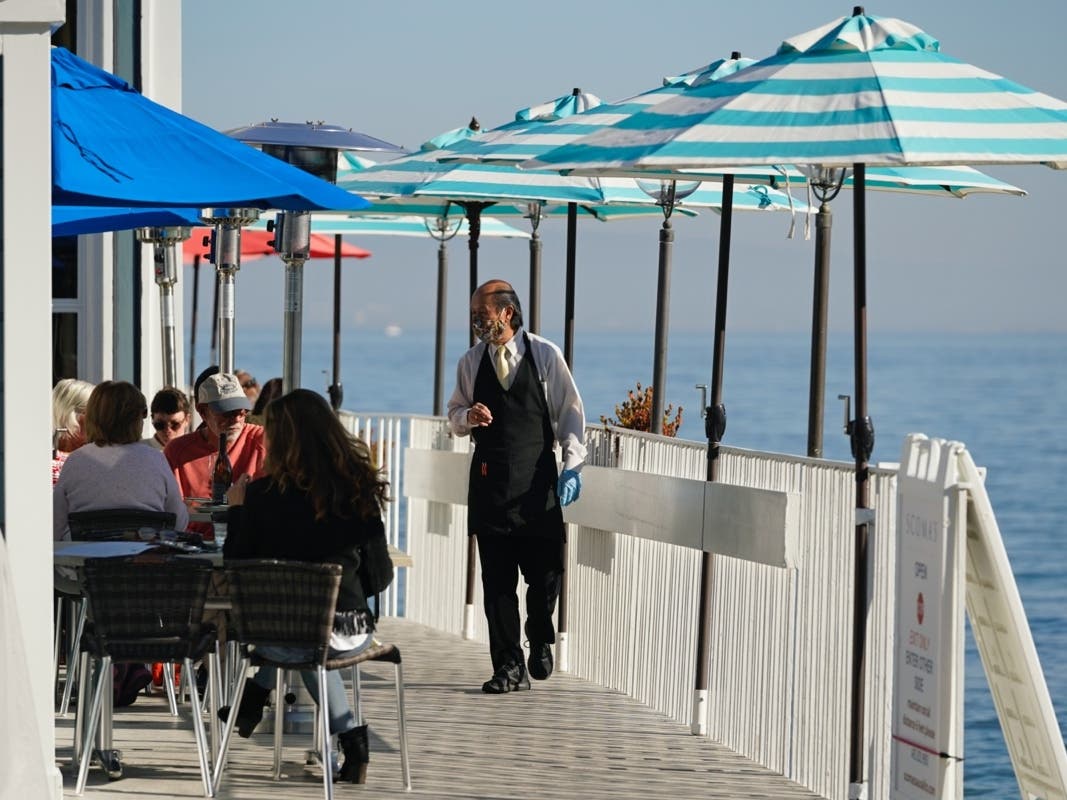 In this Dec. 4, 2020, file photo, a waiter walks past tables of people dining outdoors in Marin County at Scoma's restaurant in Sausalito, Calif. 
