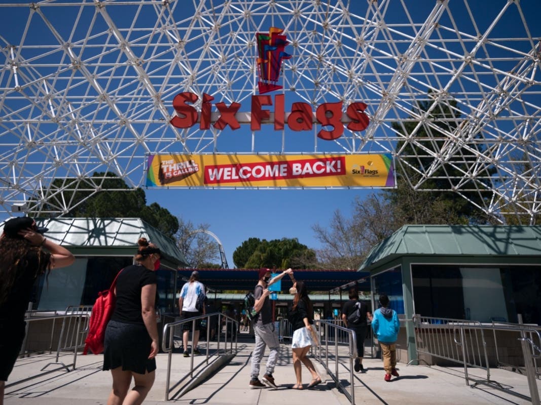 Two visitors jokingly dance as they walk underneath a "Welcome Back" sign at Six Flags Magic Mountain on its first day of reopening to members and pass holders in Valencia, Calif., Thursday, April 1, 2021. 