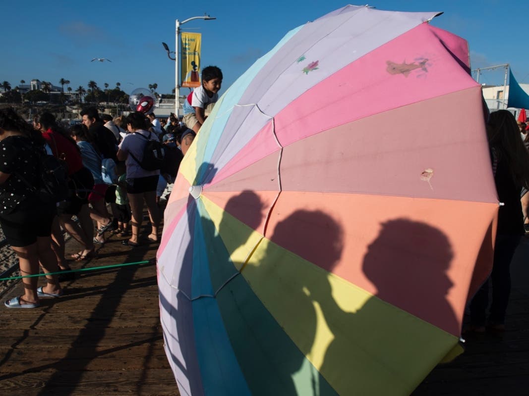 Shadow of a family taking a selfie casts on an umbrella at the pier in Santa Monica, Calif., Sunday, July 4, 2021.