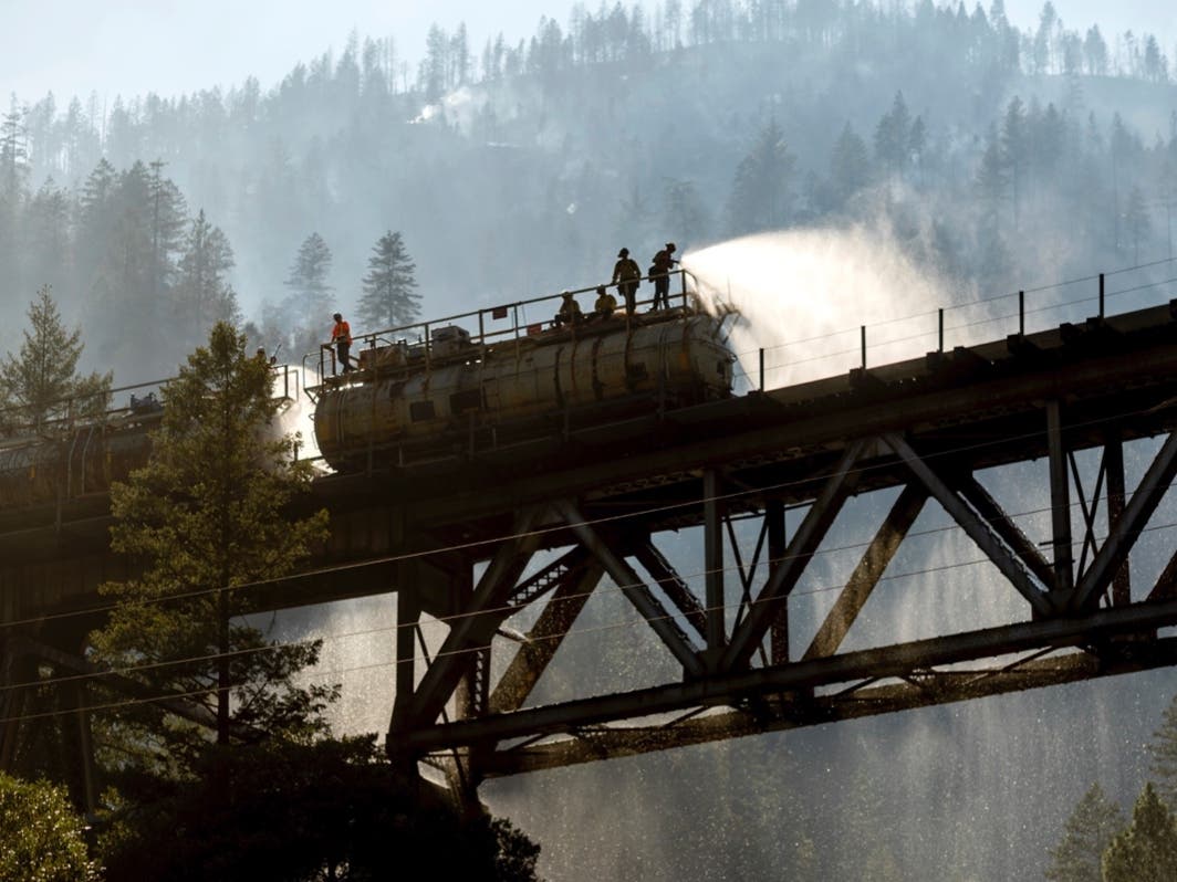 Firefighters spray water from Union Pacific Railroad's fire train while battling the Dixie Fire in Plumas National Forest, Calif., on Friday, July 16, 2021.