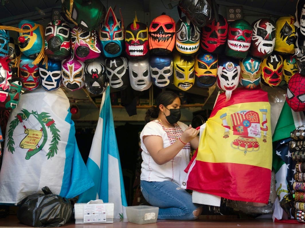 In this June 8, 2021, file photo, clerk Wendy Ramirez uses a Spanish flag to wrap souvenirs while preparing to close the store for the day on Olvera Street in Los Angeles. 