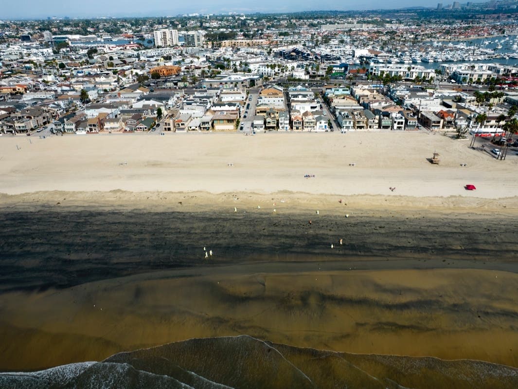In this aerial image taken with a drone, workers in protective suits clean the contaminated beach after an oil spill in Newport Beach, Calif., on Wednesday, Oct. 6, 2021. 