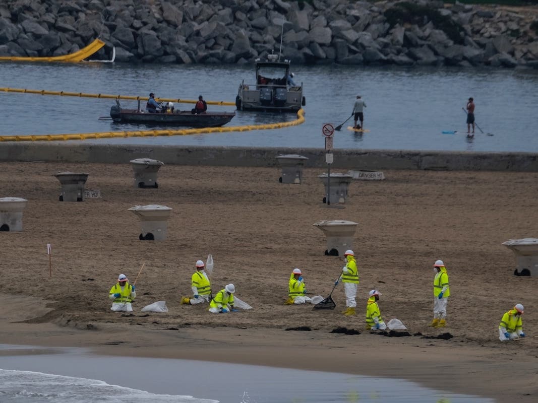 Boats deploy floating barriers known as booms in a water channel as workers in protective suits clean the contaminated beach in Corona Del Mar after an oil spill in Newport Beach, Calif.