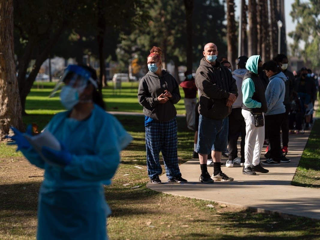 People wait in line for a COVID-19 test as medical assistant Leslie Powers, foreground, distributes results at a testing site in Long Beach Thursday.