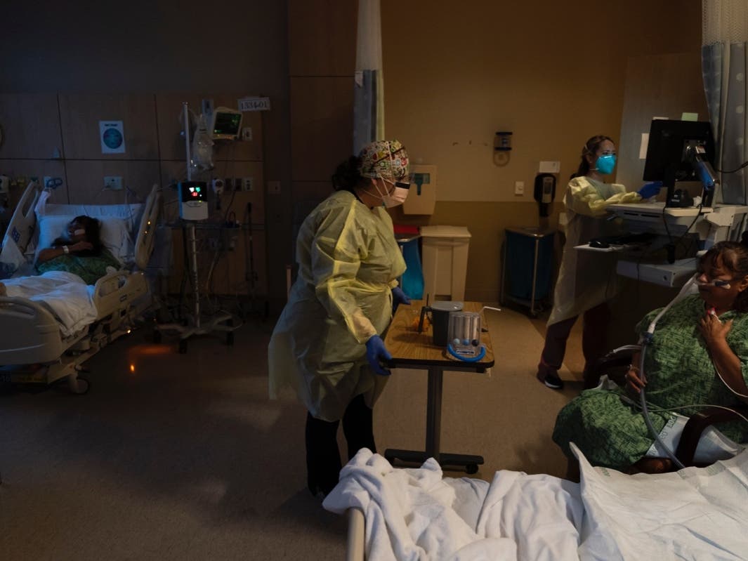 Registered nurse Nvard Termendzhyan (center) sets up a table for Linda Calderon (right) as her twin sister Natalie Balli (left) rests in her bed in a COVID-19 unit at Providence Holy Cross Medical Center in Los Angeles.