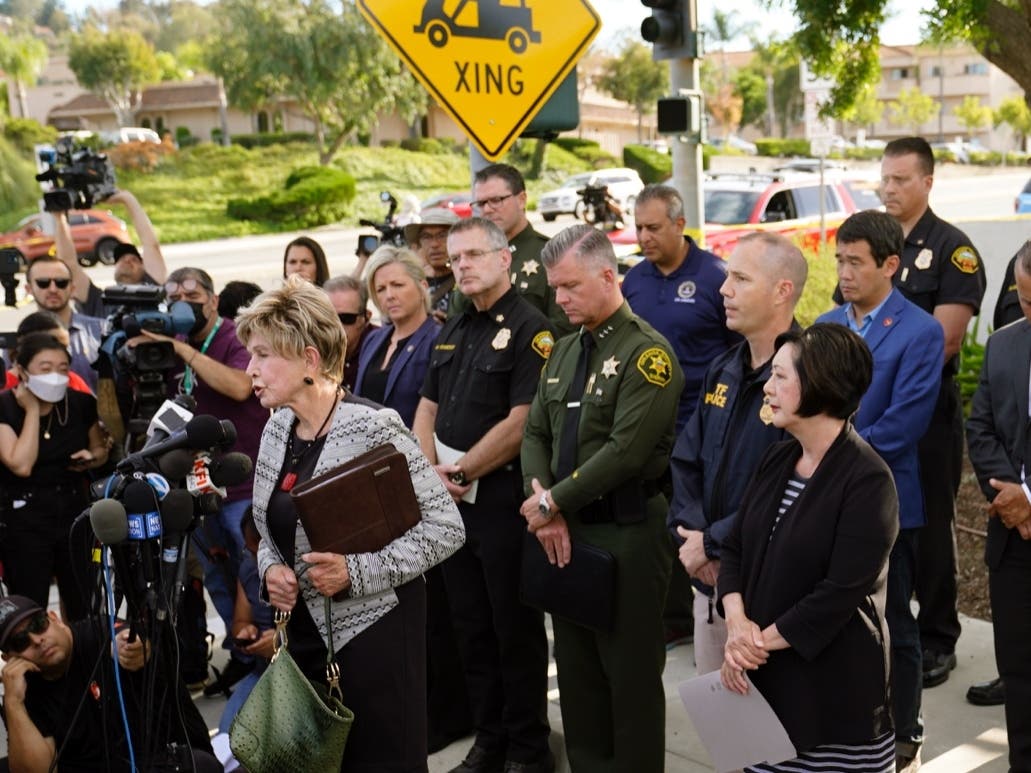 Laguna Woods Mayor Carol Moore, front left at podium, and Orange County Board of Supervisor, Lisa Barlett, right, surrounded by law enforcement officers, hold a press conference outside the grounds og Geneva Presbyterian Church in Laguna Woods, Calif.