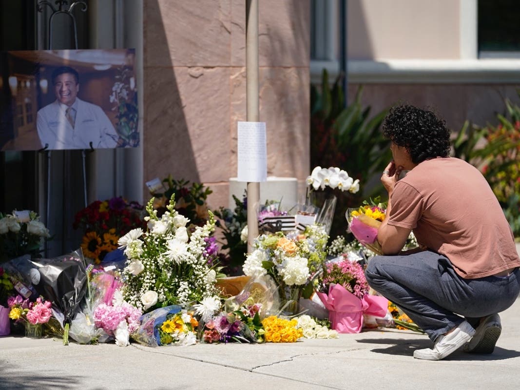 Gabe Kipers, a neighbor of Dr. John Cheng, kneels at a memorial for him outside his office building on Tuesday.