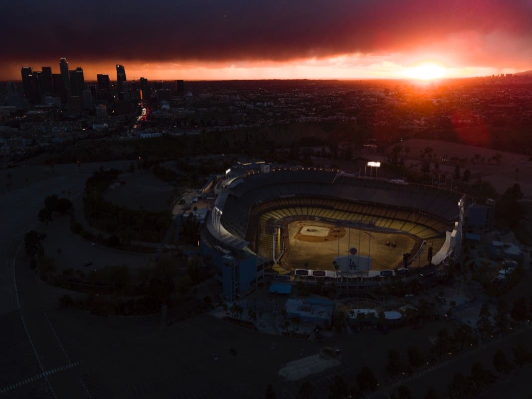 Crews are seen working on the field at Dodger Stadium as the sun sets at a distance, Tuesday, Feb. 15, 2022, in Los Angeles.