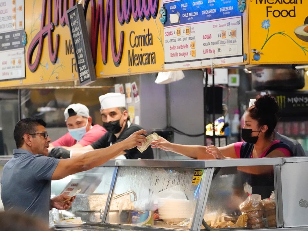 Money is exchanged at a food stand while workers wear face masks inside Grand Central Market Wednesday, July 13, 2022, in Los Angeles.