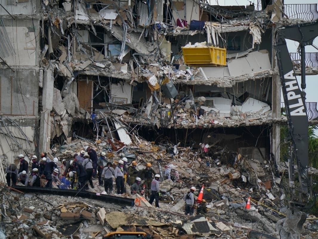 ​Search-and-rescue personnel work atop the rubble at the Champlain Towers South condo building, where scores of people remain missing after it partially collapsed a week ago.