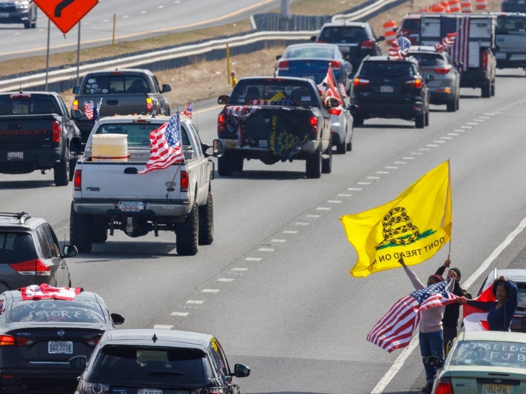People on the side of the road watch as trucks and other vehicles with the People Convoy of Truckers, protesting mandates and other issues, head South on Interstate I-270 Sunday in Frederick, Md., toward the Capital Beltway.