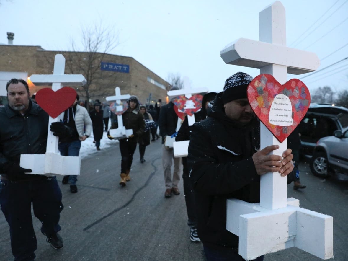 Casildo Cuevas, right, holds a victim's cross as he walks to the Aurora police station after a makeshift memorial Sunday, Feb. 17, 2019, in Aurora, Ill., near Henry Pratt Co. manufacturing company where several were killed.