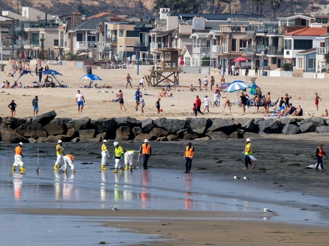 People play on the sand in the background as workers in protective suits clean the contaminated beach after an oil spill in Newport Beach on Wednesday, Oct. 6, 2021.