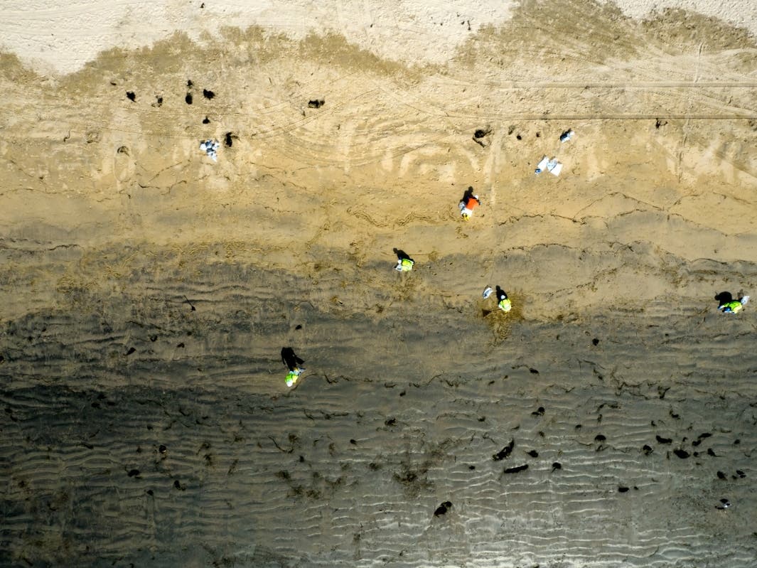 In this aerial image taken with a drone, workers in protective suits clean the contaminated beach after an oil spill in Newport Beach on Wednesday, Oct. 6.
