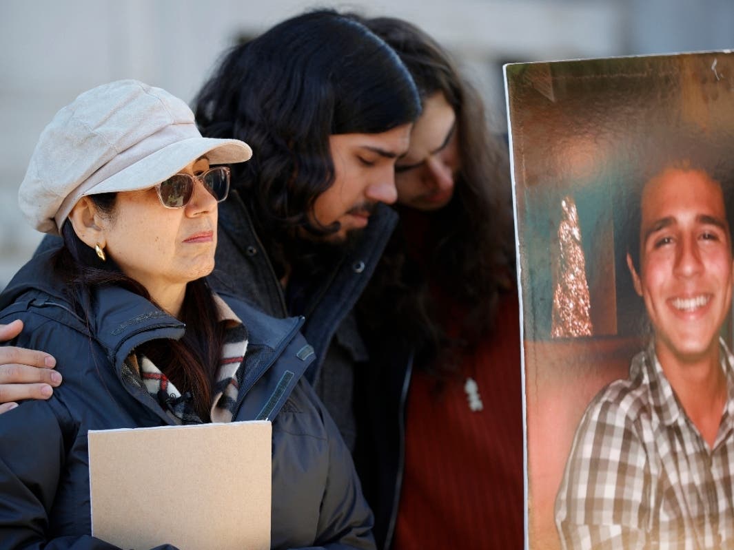 Belkis Terán, left, Daniel Paez, center, and Pedro Terán, family members of Manuel Esteban Paez Terán, known as "Tortuguita," in poster at right, embrace during a news conference, Monday, March 13, 2023, in Decatur, Ga.
