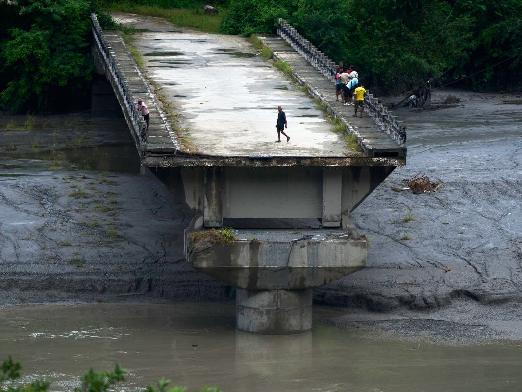 People stand on remnants of a bridge which spanned across Trishuli river and was washed away in flash floods, in Dhading District, Nepal, Sunday, Aug. 30, 2026.