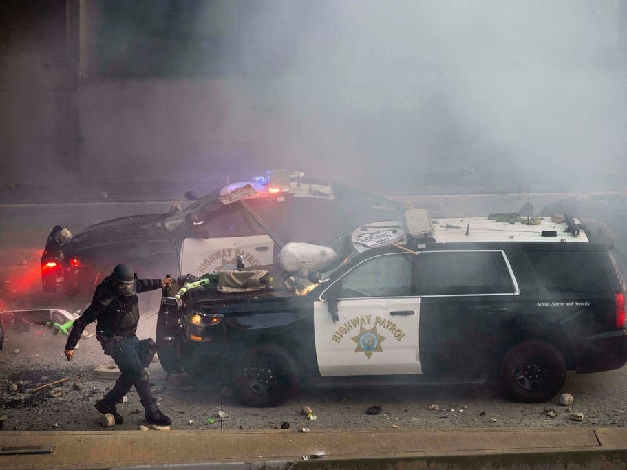 A California Highway Patrol officer pulls an electric scooter off a vehicle on a highway as protesters throw objects at the police vehicles near the Metropolitan Detention Center in downtown Los Angeles, Sunday, June 8, 2025.