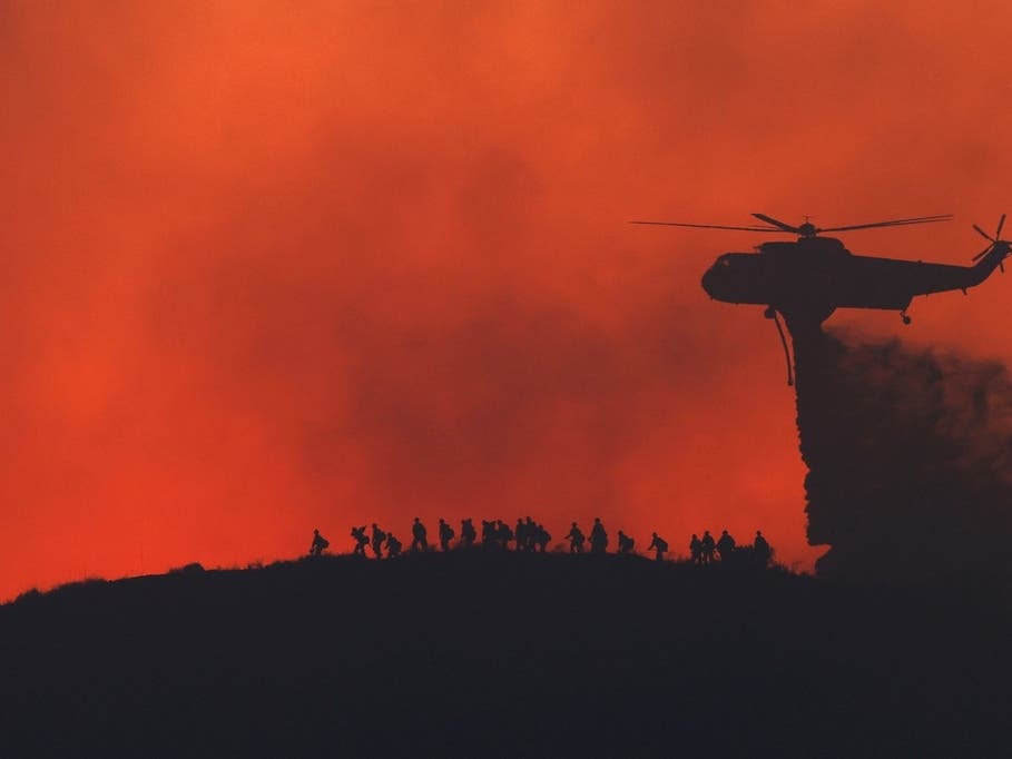 A water tanker drops water while firefighters walk below, as the Sandy Fire approaches, Tuesday, May 19, 2026, in Simi Valley.