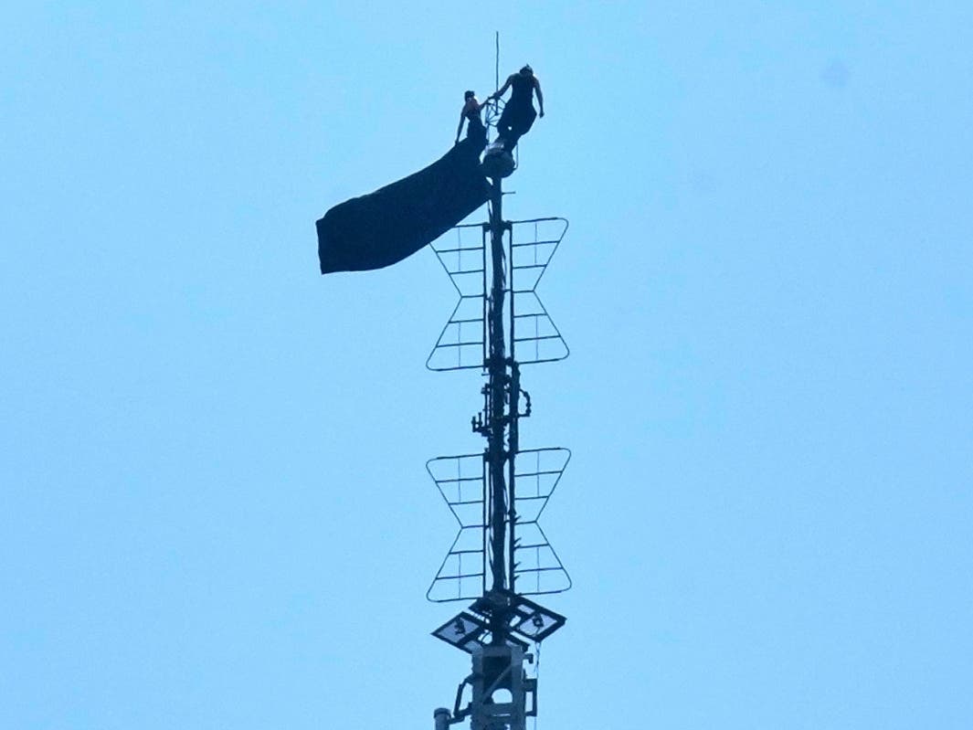 Two people stand on the tip of the antenna of the Empire State Building while holding a banner on Wednesday, July 1, 2026.