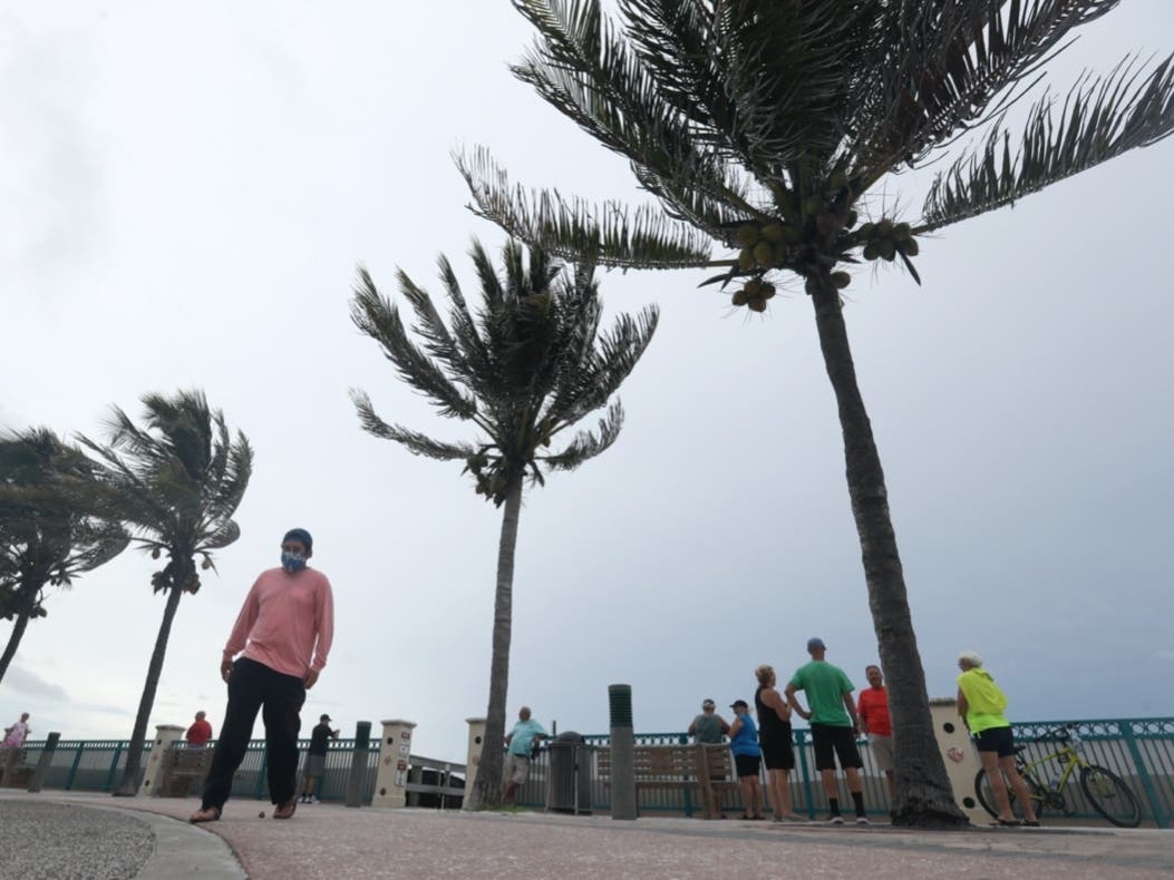 People gather to watch the strong waves on the beach as palm trees sway in the wind, Sunday, Aug. 2, 2020, in Vero Beach, Fla. Isaias weakened from a hurricane to a tropical storm late Saturday afternoon.