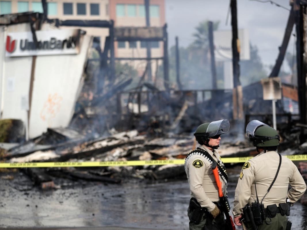 San Diego County sheriff officers stand guard in front of a burning bank building after a protest over the death of George Floyd, Sunday, May 31, 2020, in La Mesa, Calif. Protests were held in U.S. cities over the death of Floyd, a black man who died afte