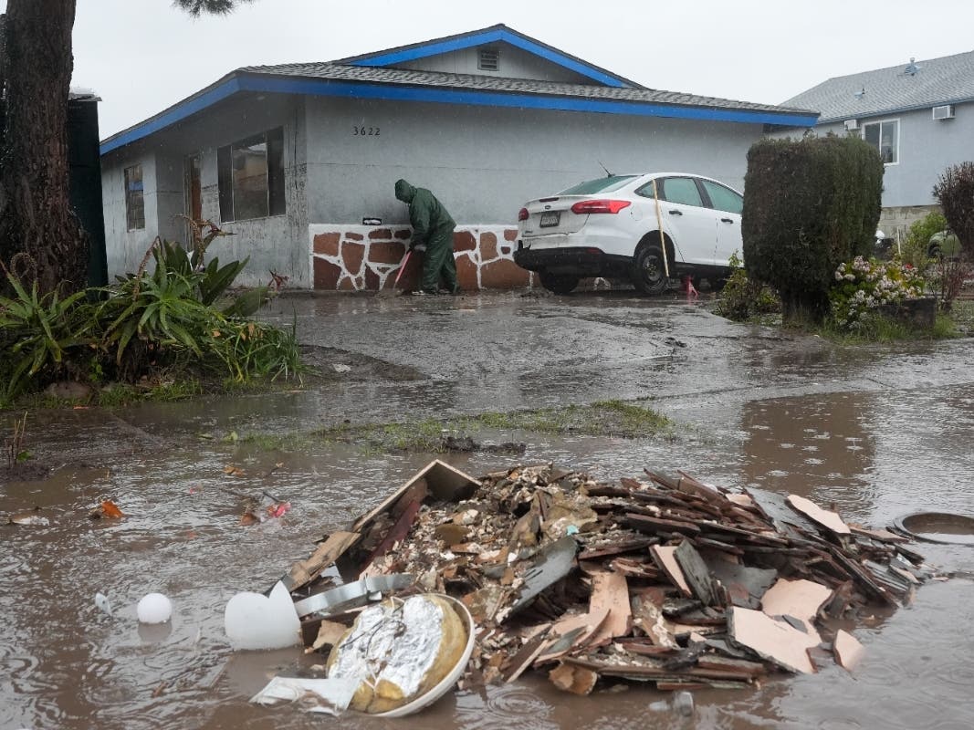 Ruben Gomez digs away some of the mud and flood debris that engulfed his parents' home in the previous rainstorm as more rain falls, Thursday, Feb. 1, 2024, in San Diego. 