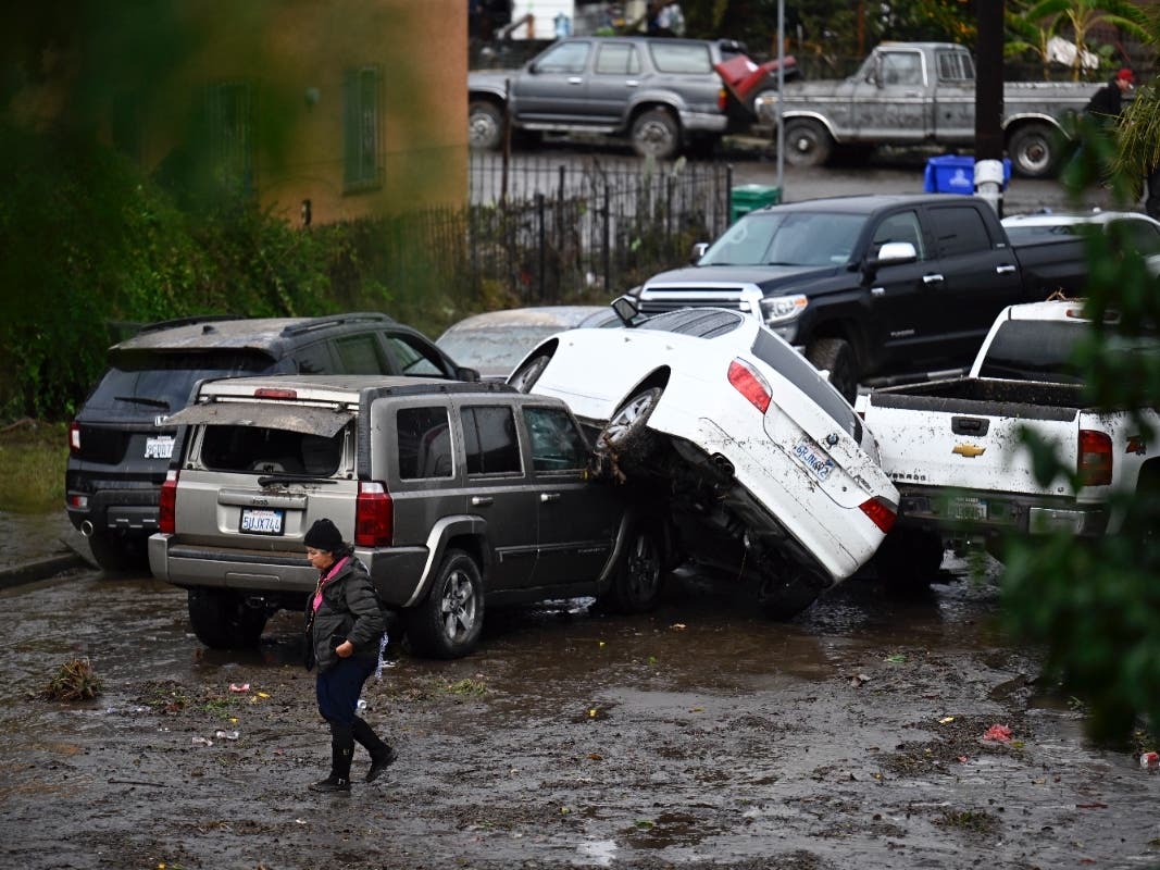 A woman walks by cars damaged by floods during a rainstorm in San Diego on Monday, Jan. 22, 2024.