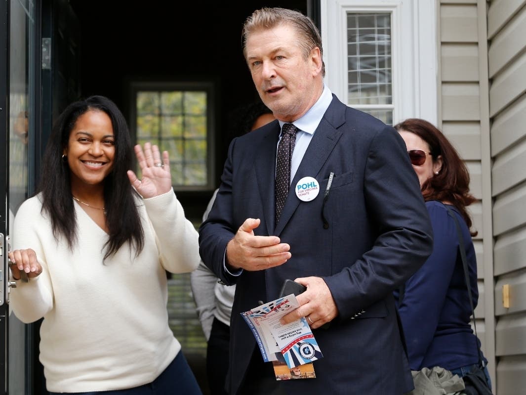 Actor Alec Baldwin, center, points out a throng of media as he talks to Kristin Goodlett as he walks with Amanda Pohl, candidate for Virginia Senate District 11 in her neighborhood in Midlothian, Virginia.