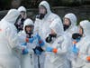 Workers from a Servpro disaster recovery team wearing protective suits and respirators are given supplies as they line up before entering the Life Care Center in Kirkland, Washington, to begin cleaning and disinfecting the facility.