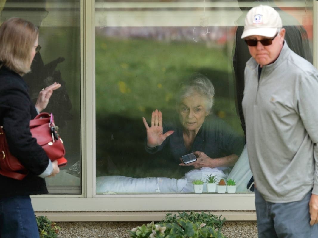 Judie Shape (center), who has tested positive for the coronavirus but isn't showing symptoms, presses her hand against her window after a visit with her family through the window of Life Care Center in Kirkland, Washington.